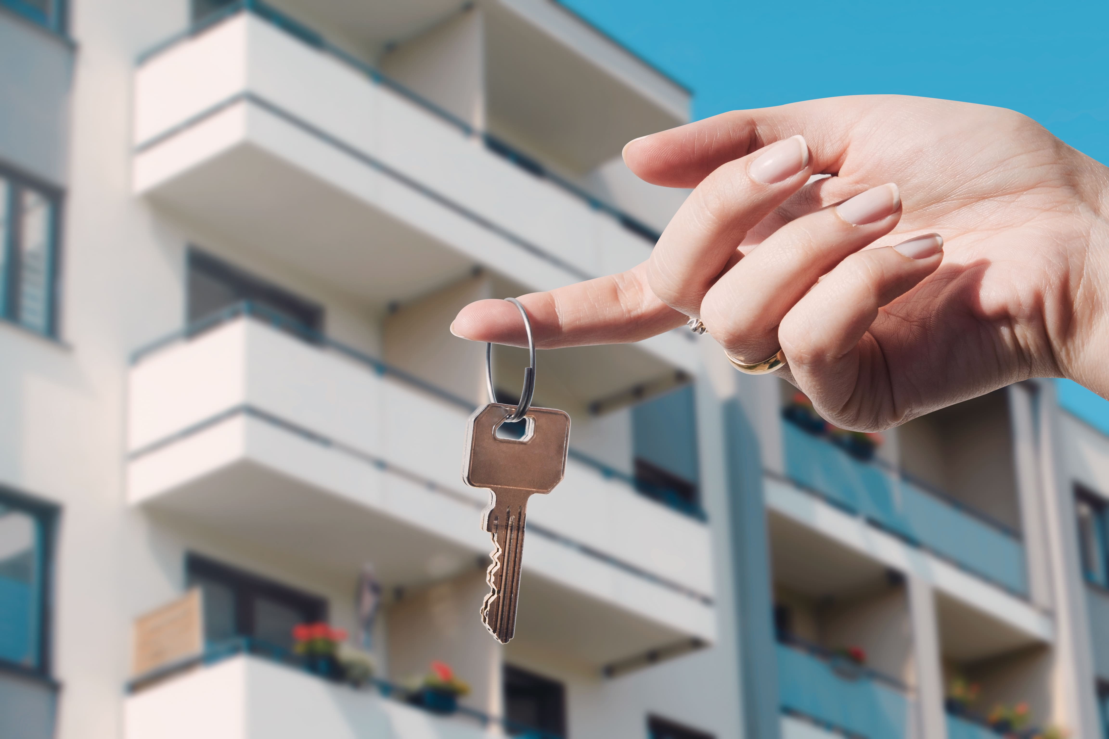 Mão segurando chave de apartamento com prédio residencial ao fundo, simbolizando locação por temporada.