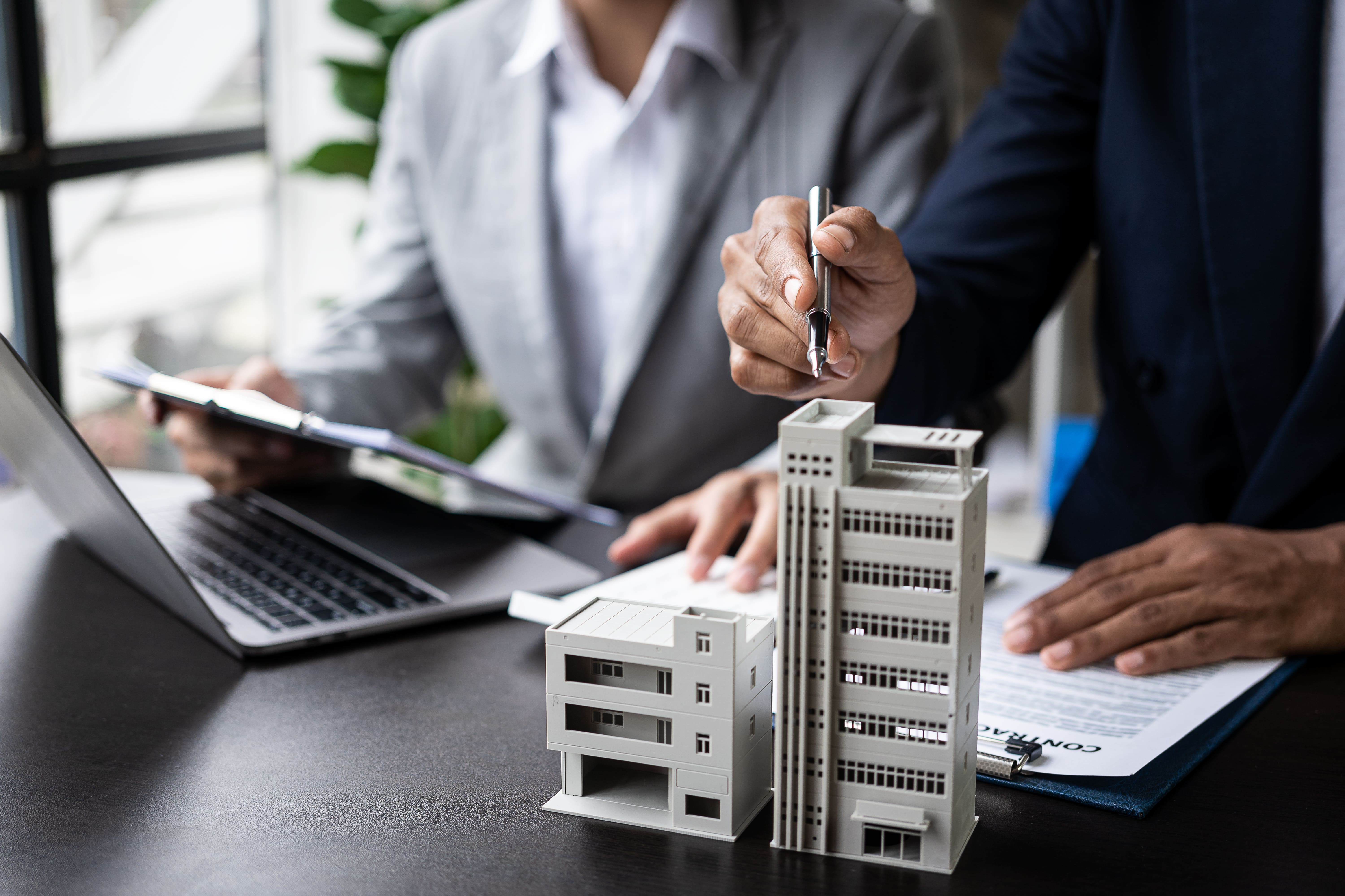 Profissionais discutindo contrato imobiliário com maquete de edifícios sobre a mesa, indicando uma discussão sobre Airbnb em condomínios